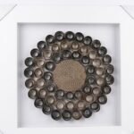 Framed 3D wall art with dark rolled paper circles and woven center in a distressed white frame in Lagos, Nigeria