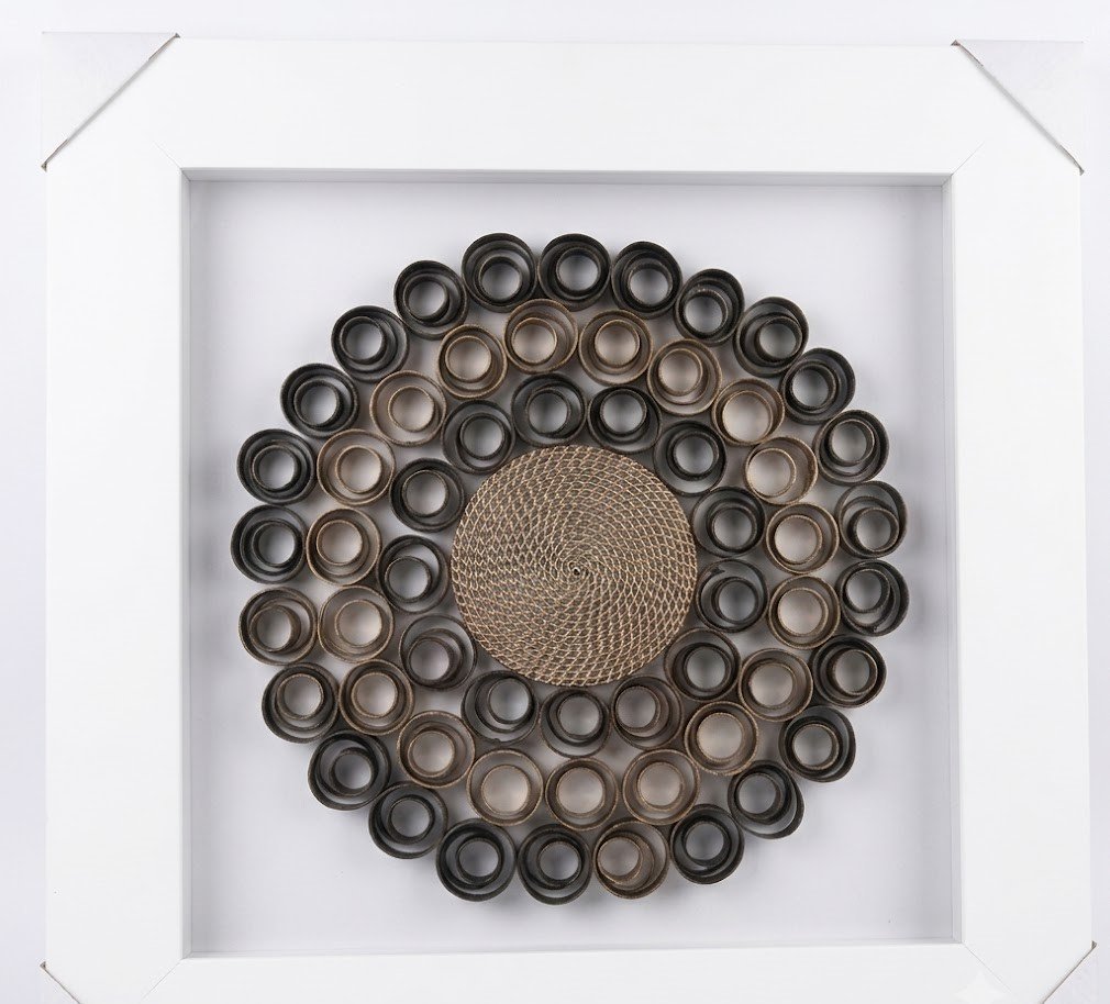 Framed 3D wall art with dark rolled paper circles and woven center in a distressed white frame in Lagos, Nigeria