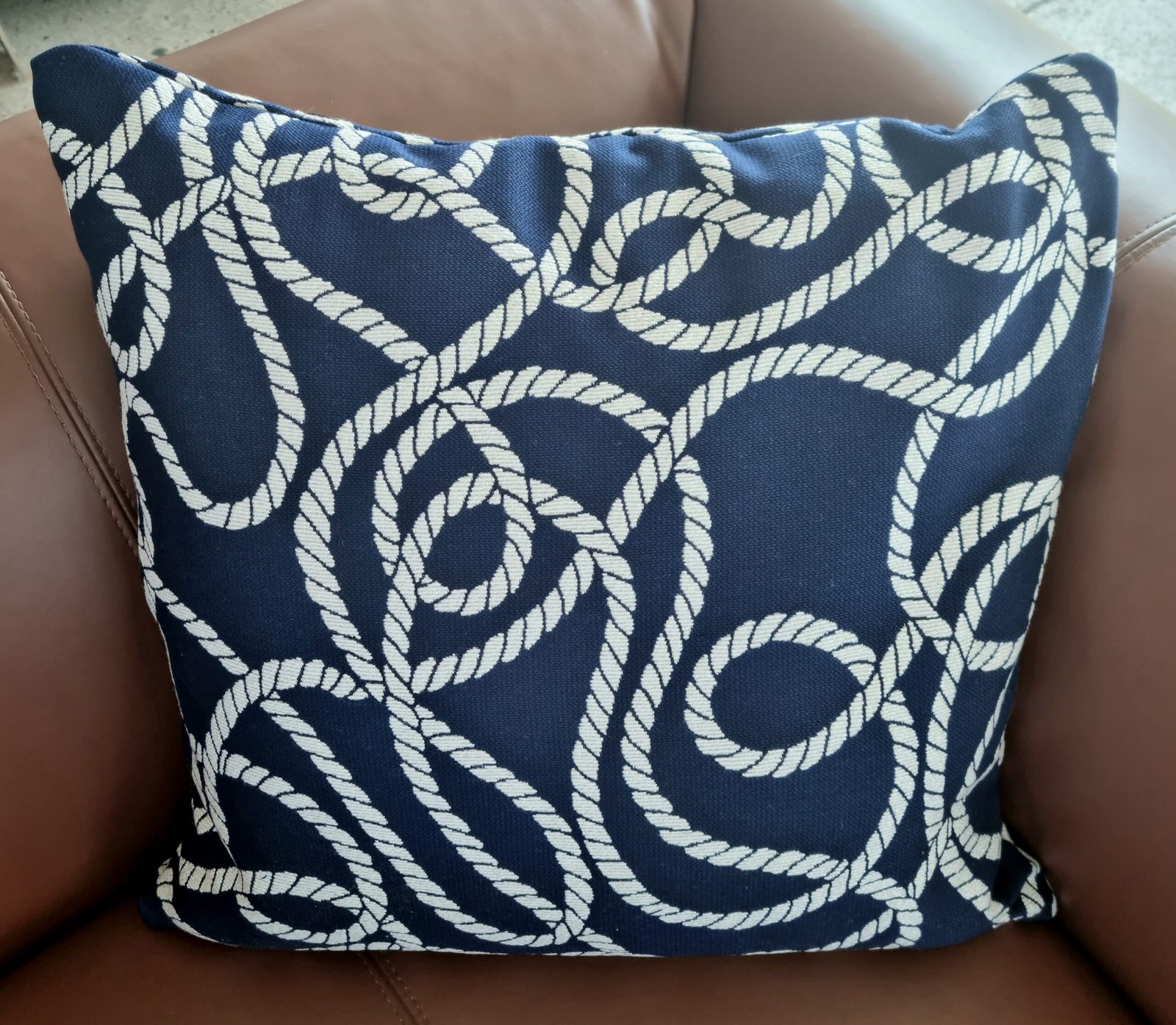 Navy blue outdoor cushion with white marine rope knot pattern, packaged in a clear plastic bag for delivery, Lagos Navy blue outdoor cushion with white marine rope knot pattern, packaged in a clear plastic bag for delivery, Lagos